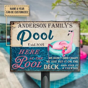 May include: A blue and white metal sign with the text "Anderson Family's Pool Estd. 2021" and a pink flamingo holding a cocktail in a glass. The sign also says "Here at the Pool We don't hide crazy we just put it on the deck and give it a cocktail."