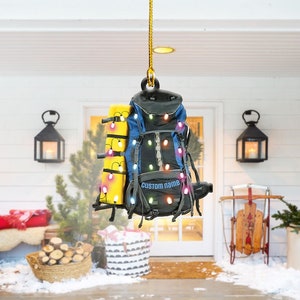 May include: A blue and black backpack with a yellow sleeping bag strapped to it. The backpack is decorated with colorful Christmas lights and the text "CUSTOM NAME".