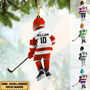 May include: Personalized hockey player Christmas ornament with a red, white, and black jersey. The ornament features the name "William" and the number "10" on the back. The ornament is hanging from a Christmas tree.