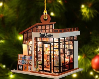 May include: A miniature wooden model of a bookshop with a glass storefront and a sign that reads "Book Store". The model is decorated with lights and bookshelves filled with books. It is hanging from a gold string, suggesting it is an ornament.