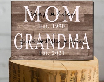 May include: A wooden sign with the words "Mom" and "Grandma" in white letters. The sign also includes the names "Emmy Nolan" and "Jacob Kyle Erin" with hearts between the names. The sign also includes the text "Est. 1990" and "Est. 2021".