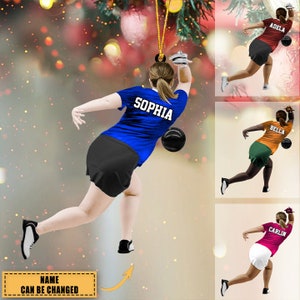 May include: A personalized bowling ornament featuring a woman in a blue shirt and black shorts, throwing a bowling ball. The ornament is customizable with a name, such as "Sophia", and can be used as a Christmas tree decoration or a gift for a bowling enthusiast.