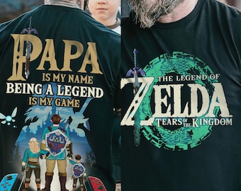 May include: Two dark green t-shirts. One features the text "PAPA IS MY NAME BEING A LEGEND IS MY GAME" with a family graphic. The other displays "THE LEGEND OF ZELDA TEARS OF THE KINGDOM" in green and white.