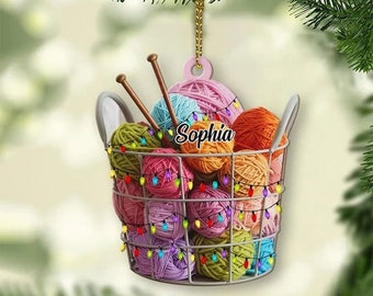 Pode incluir: Uma cesta de arame branca cheia de novelos de lã coloridos e decorada com luzes piscando. A cesta está pendurada em uma corda e tem o nome "Sophia" escrito nela.