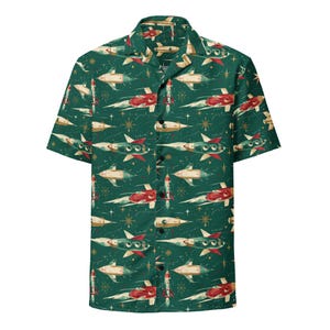 May include: A short-sleeved shirt with a retro space-themed pattern. The shirt has a dark green background with repeating illustrations of rockets, stars, and other space-age elements in red, white, and beige.