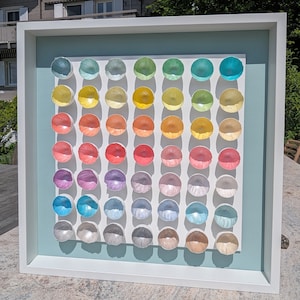 May include: A framed artwork featuring a rainbow gradient of 49 small, round, iridescent, ceramic bowls arranged in a grid pattern.