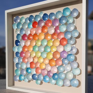 May include: A framed artwork featuring a rainbow gradient of colorful round shapes, resembling a honeycomb pattern. The shapes are made of paper and are arranged in a square formation.