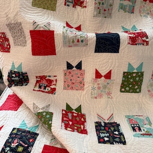 May include: A white Christmas quilt with a repeating pattern of gift boxes. The boxes are in various colours and patterns, including red, green, and blue, with decorative bows. The quilt is machine-stitched with a swirling pattern.