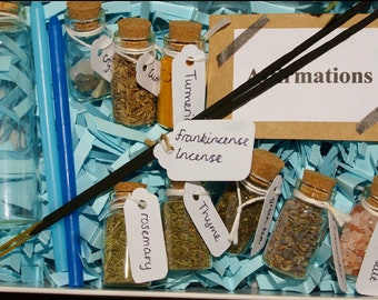 Può includere: Una scatola regalo piena di piccoli barattoli di vetro contenenti erbe e spezie, tra cui rosmarino, timo, lavanda e sale rosa. La scatola contiene anche due bastoncini di incenso e un biglietto che dice "Affirmations".