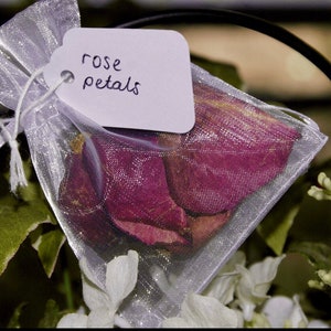Pu&ograve; includere: Un sacchetto di organza bianco pieno di petali di rosa secchi. Il sacchetto ha un'etichetta bianca attaccata che dice "rose petals".