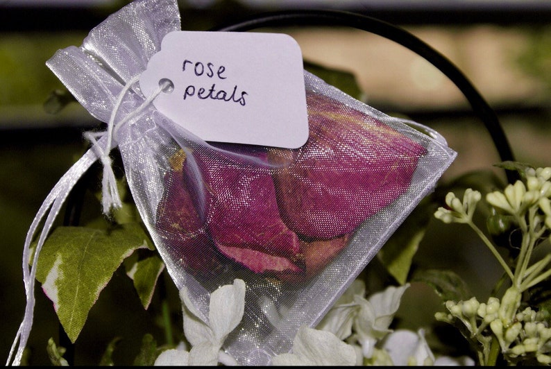 Pu&ograve; includere: Un sacchetto di organza bianco pieno di petali di rosa secchi. Il sacchetto ha un'etichetta bianca attaccata che dice "rose petals".