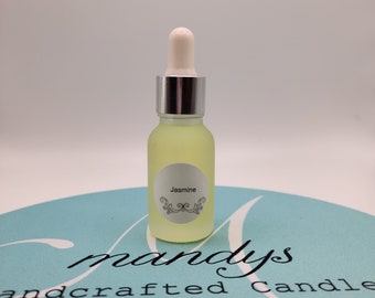 May include: A clear glass bottle with a silver cap and a white dropper. The bottle is filled with a light yellow liquid. The label on the bottle says "Jasmine". The bottle is sitting on a light blue surface with the text "mandys handcrafted candle" printed on it.