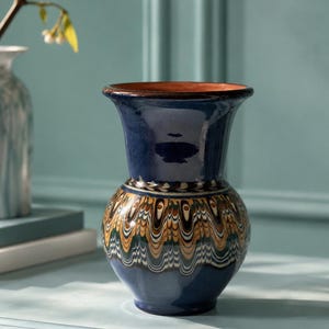 May include: A ceramic vase with a flared rim and a rounded body, featuring a glossy dark blue glaze on the top and bottom sections, and a central band decorated with intricate, multi-colored marbled patterns in brown, green, and white.