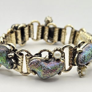 May include: A vintage gold-toned bracelet featuring heart-shaped iridescent glass stones and small faux pearls. The bracelet has a decorative link design and a secure clasp. A unique piece of jewelry.