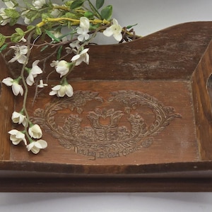 May include: A wooden serving tray with carved floral details and the text "Not by Bread Alone." The tray has handles and is decorated with white flowers and green leaves.