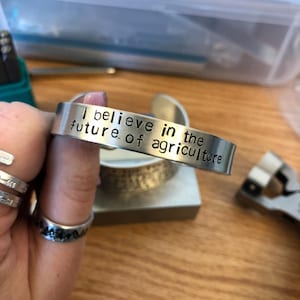 May include: A silver bracelet with the inscription "I believe in the future of agriculture".