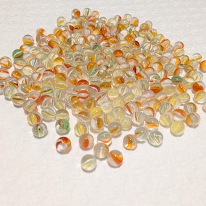 May include: A collection of clear glass marbles with orange, yellow, red, and green swirls. The marbles are scattered, showcasing their colorful patterns and translucent quality. These decorative marbles are suitable for games or crafts.