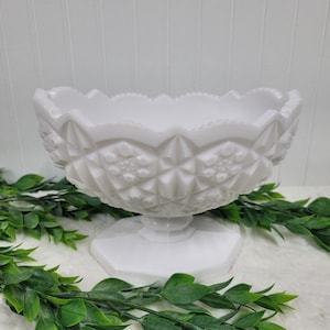 May include: White milk glass pedestal bowl with a diamond pattern. The bowl has a scalloped edge and a footed base.