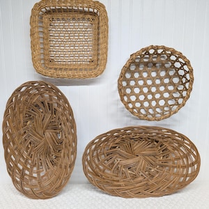 May include: Four woven wicker baskets in various shapes. There is a square basket, a round basket, and two oval baskets. The baskets are all a light brown color and have a woven design. The baskets are displayed against a white background.