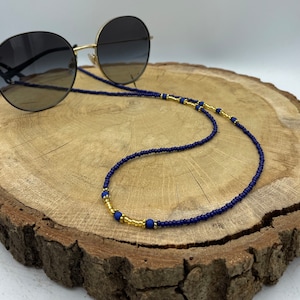 Op de afbeelding: Een brilketting van donkerblauwe en gouden kralen. De ketting is gemaakt van kleine, ronde kralen en heeft een gouden accent in het midden.