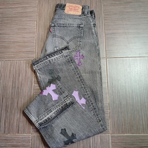 Op de afbeelding: Grijze denim jeans met geborduurde kruisen in zwart en paars. De jeans hebben een klassiek vijf-zakken ontwerp, een Levi's merklabel en een rechte pijp.
