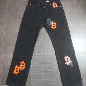 Könnte beinhalten: Schwarze Jeans aus Denim mit orangefarbenen Bitcoin-Symbolen auf den vorderen und hinteren Taschen.