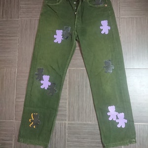 May include: Green denim jeans with multiple purple and black bear appliques.