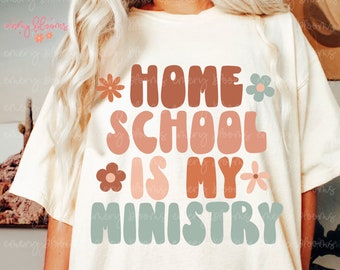 May include: Cream-colored t-shirt with the text "HOME SCHOOL IS MY MINISTRY" in brown, peach, and teal lettering. The design includes floral accents in coordinating colors. A casual, comfortable tee.
