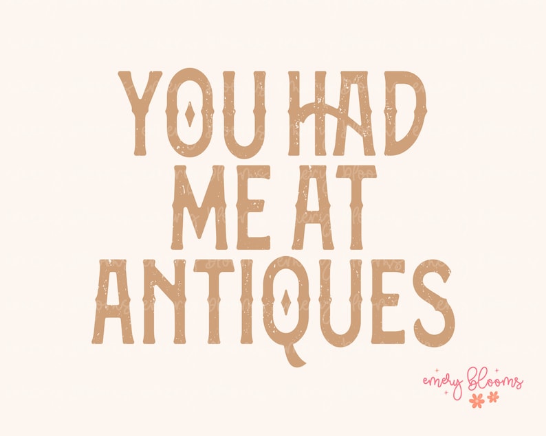 May include: A beige print with the words "YOU HAD ME AT ANTIQUES" in a brown, textured font. The bottom right corner features the text "emery blooms" in a script font with floral accents.