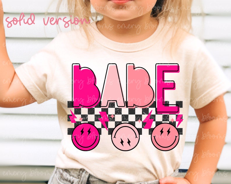 May include: A white t-shirt with the word "BABE" in pink and white letters. The letters are outlined in black and have a checkered pattern behind them. There are three pink smiley faces with lightning bolts below the word.
