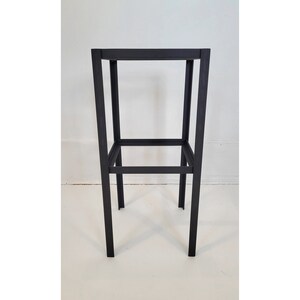 May include: A black metal stool with a simple, rectangular design. The stool has two shelves for storage or display.