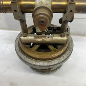May include: A vintage brass and silver surveying instrument with a telescope and a graduated circle. The instrument is used for measuring angles and distances.
