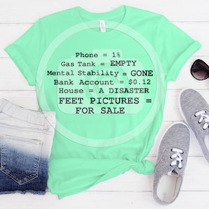Könnte beinhalten: Ein hellgrünes T-Shirt mit einer humorvollen Grafik, auf der steht: "Telefon = 1 %, Tank = Leer, Mentale Stabilität = Weg, Bankkonto = 0,12 €, Haus = Eine Katastrophe, Fußbilder = Zu verkaufen".
