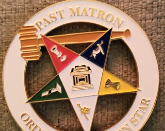 May include: A white, gold, and multi-colored metal pin with a five-pointed star in the center. The star is surrounded by a circle with the words "Past Matron Order of Eastern Star".