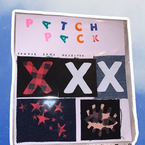 Puede incluir: Un conjunto de parches para planchar con una variedad de diseños, incluyendo una "X" de cuadros rojos y negros, una "X" blanca, una "X" de mezclilla azul, un patrón de estrellas rojas y un diseño de ojo marrón y beige. Los parches están empaquetados en una manga de plástico transparente con el texto "Patch Pack" y "Rework your wardrobe" impreso en la parte delantera.