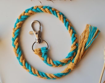 May include: A braided keychain with a turquoise and mustard yellow color scheme. The keychain has a silver metal clasp.