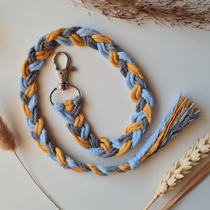May include: A braided key chain with a silver key ring. The chain is made of blue and yellow yarn.