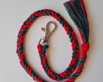 May include: A braided key chain with a red and green color scheme. The chain has a silver metal clasp and a tassel at the end.
