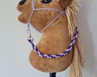 May include: A brown plush horse head with a purple and lavender braided rope halter. The horse has a long, blonde mane and tail. The horse head is mounted on a black stick.