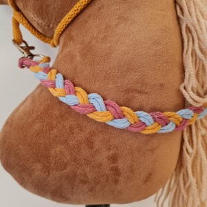 May include: A brown plush horse head with a braided rope halter in yellow, pink, and blue. The horse has a long, white mane.