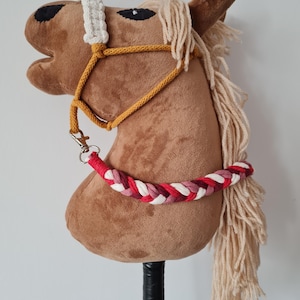 May include: Brown plush horse head with a white and yellow bridle and a red, white, and pink braided rope attached to the bridle. The horse head is mounted on a black stick.