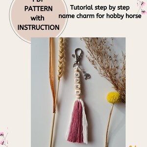Może przedstawiać: Samouczek krok po kroku, jak zrobić brelok z imieniem dla konia hobbystycznego. Brelok jest wykonany z drewnianych koralików, frędzli i srebrnego kółka na klucze. Korale są pomalowane literami "NAME".
