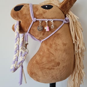 May include: A brown plush horse head with a lavender braided rope halter and a white and lavender braided rope lead. The halter has three charms attached: a silver horseshoe, a silver star, and a pink unicorn.