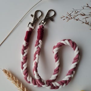 May include: A braided cord with white and burgundy colored rope, with silver clasps on each end.