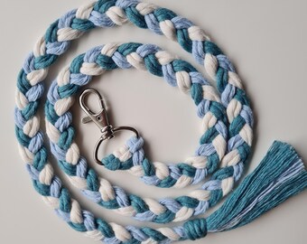 May include: A braided lanyard with a light blue, white, and teal color scheme. The lanyard has a silver metal clasp and a teal tassel.