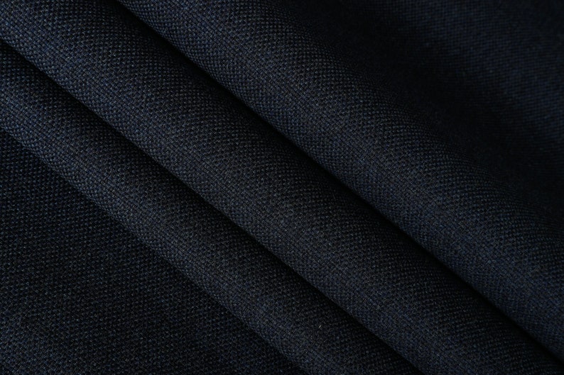 May include: Close-up of a dark blue fabric with a textured weave. The fabric is folded in a way that shows the texture and depth of the material.