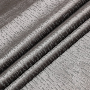 May include: Close-up of a gray fabric with a subtle textured pattern. The fabric is folded in a few places, showing the texture and sheen.