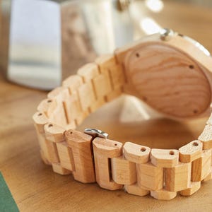 May include: A wooden wristwatch with a light brown wood band and a light brown wood face. The watch is lying on a wooden surface.