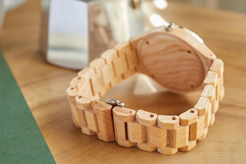 May include: A wooden wristwatch with a light brown wood band and a light brown wood face. The watch is lying on a wooden surface.