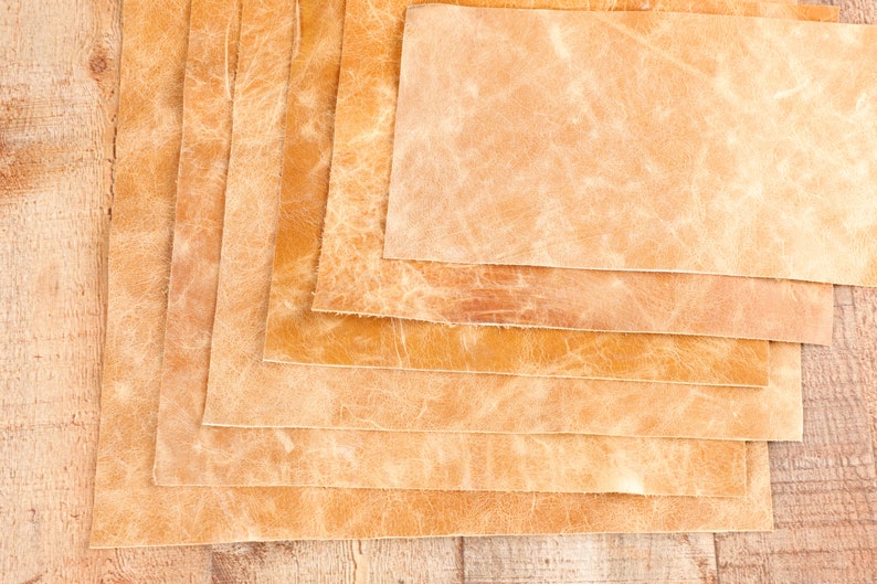 May include: Stack of six pieces of light brown leather, each with a different texture and shade of brown.